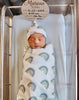 Newborn in bassinet wrapped in swaddle blanket & hat with mulit-shades of blue rainbows. Bassinet sheet light blue.  