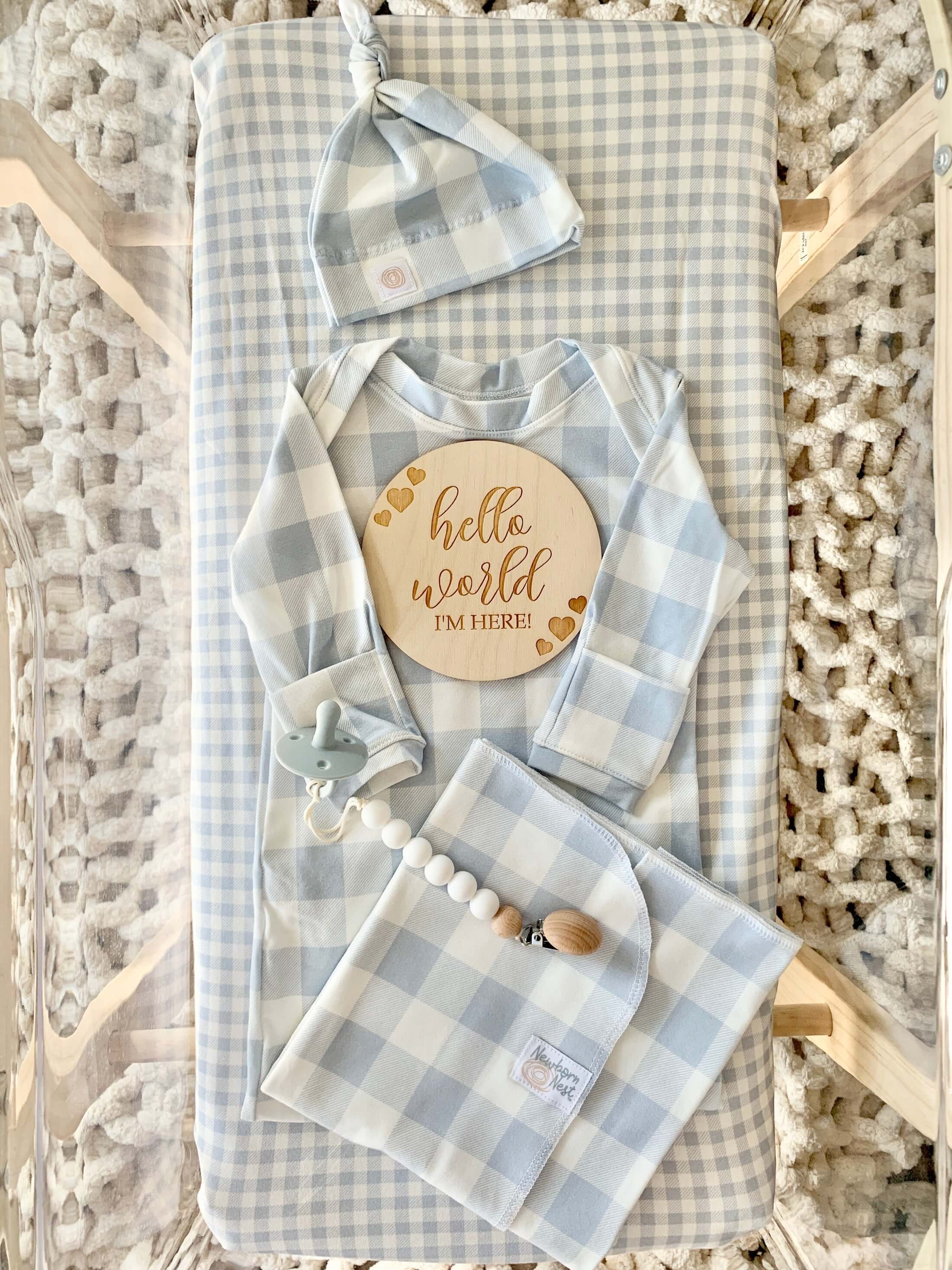 Light blue buffalo print swaddle blanket. newborn gown & headband bow.  Light blue bassinet sheet.  Displayed in a hospital bassinet. 